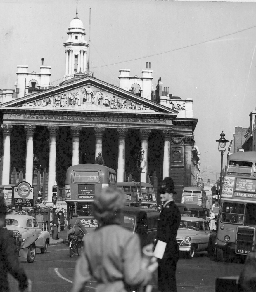 Pedestrians and cars crowd a street in front of a large building.