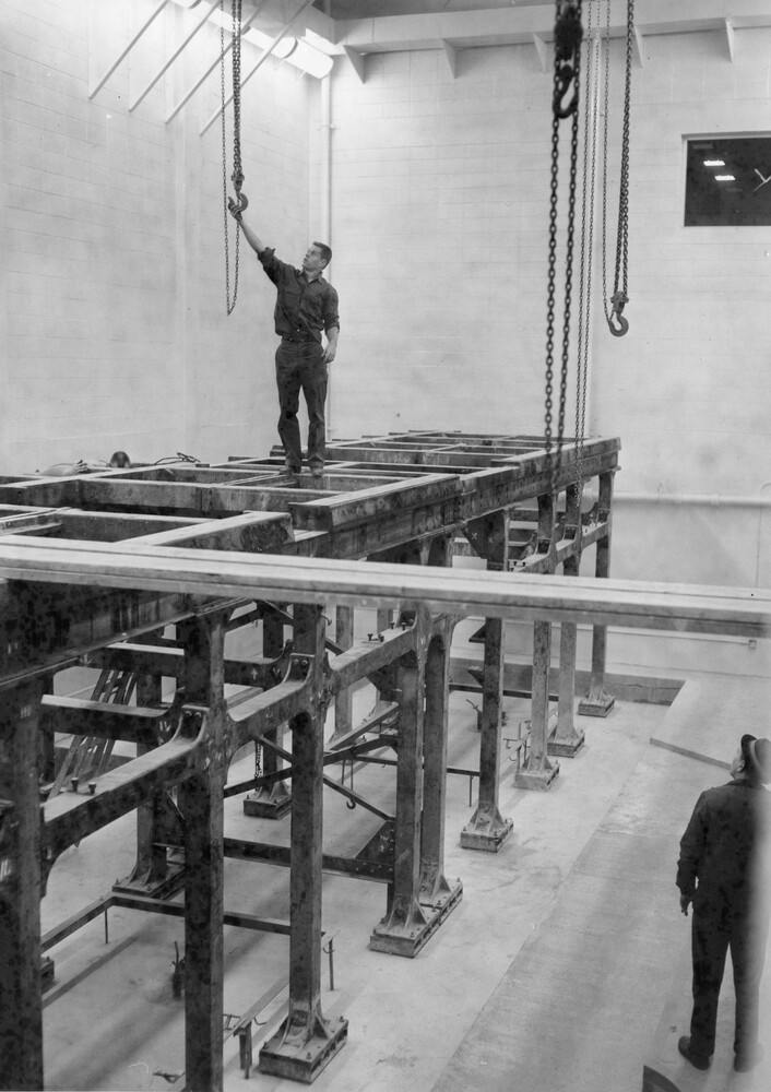 A man stands atop a steel grid structure as another man looks on.