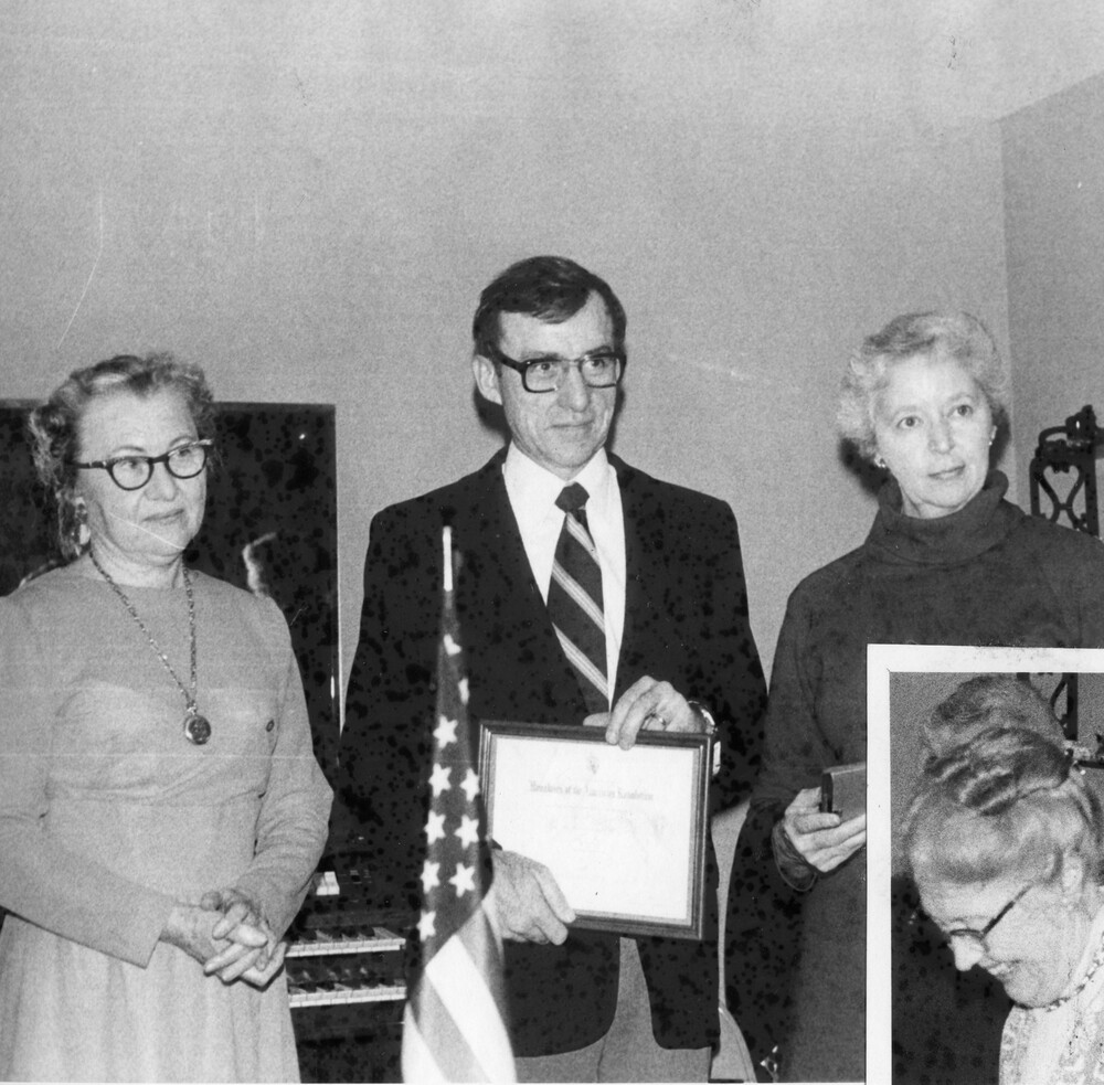 Two women with a man holding an award; a woman inset at bottom right.