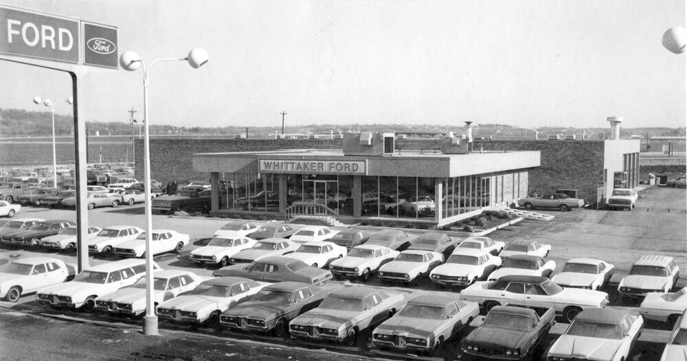 Photo of car lot with building and rows of cars; Ford sign