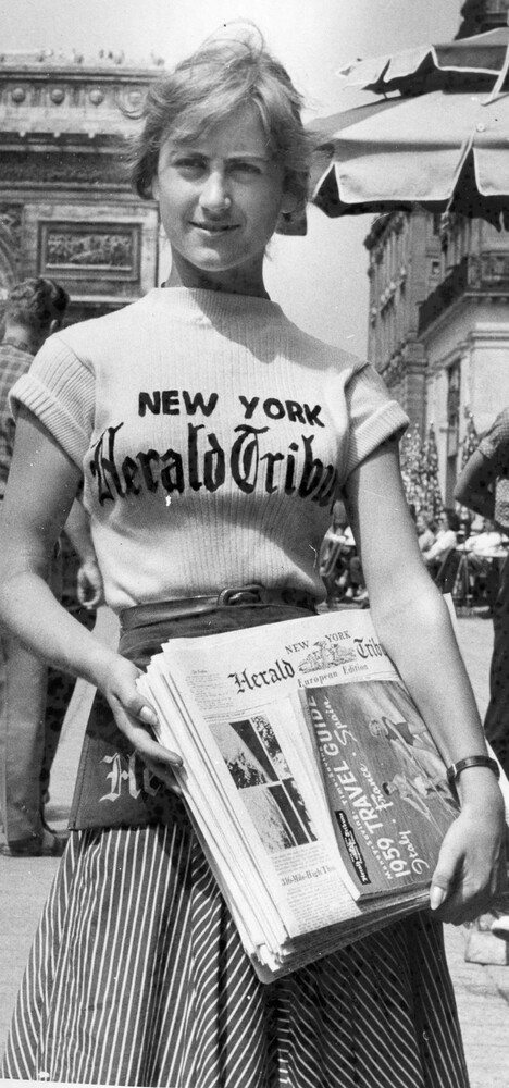 A woman holding a bundle of newspapers.