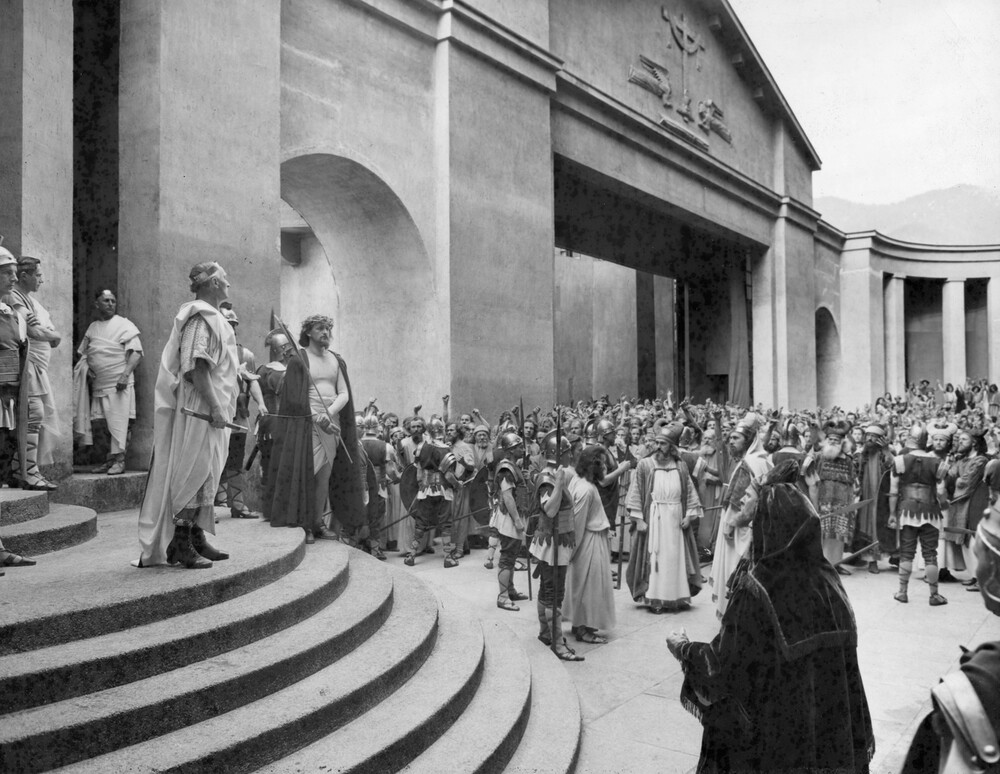 Two men standing on a theater stage in front of a crowd of people.