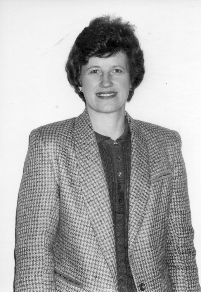 Photo of woman with short hair, wearing dark blouse and houndstooth jacket