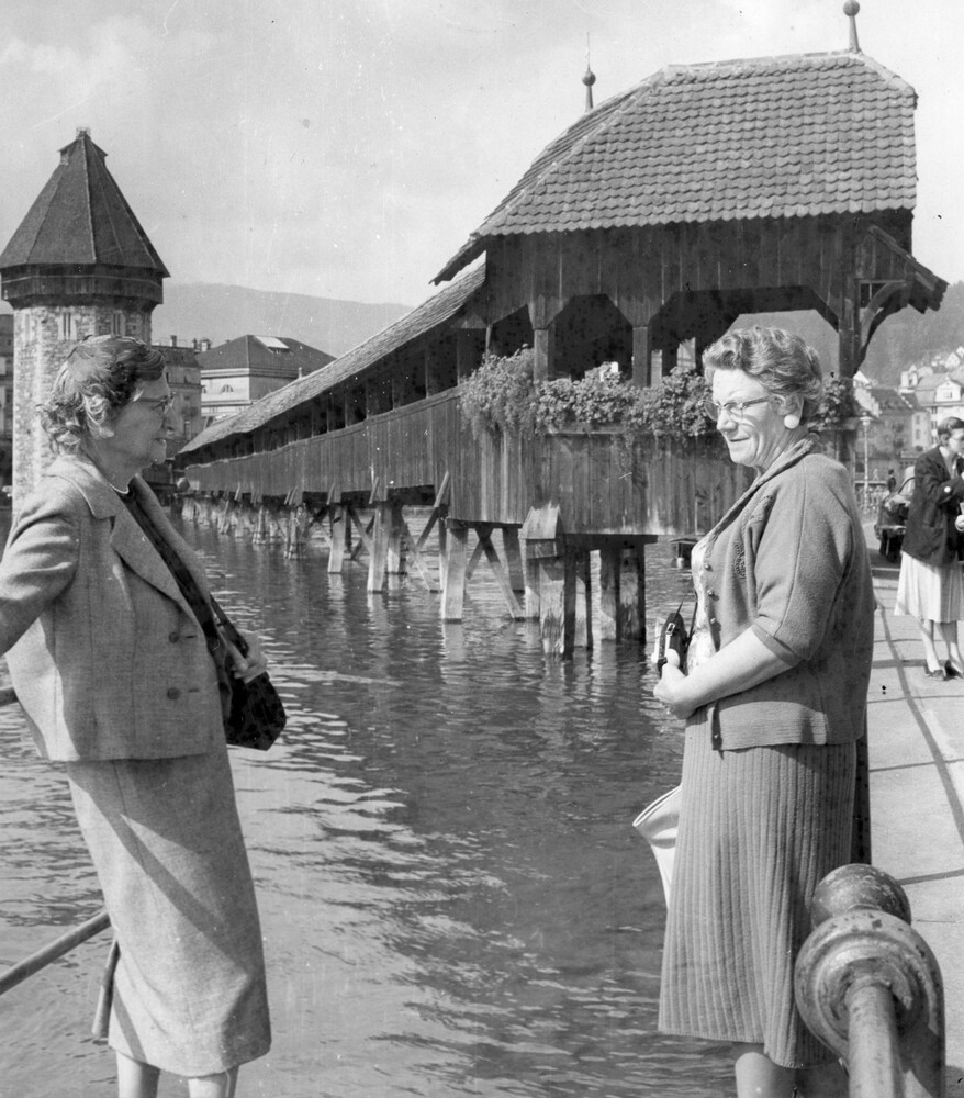 Two women near a covered bridge over water.