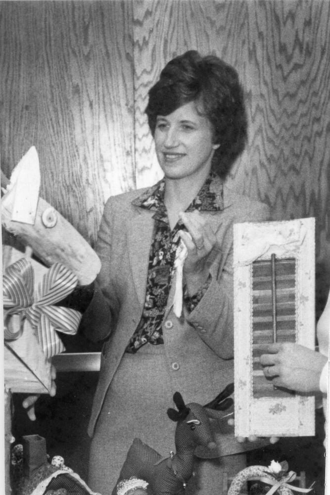 Woman in suit stands behind table of crafts