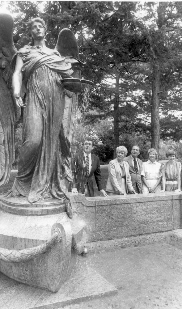 Five people stand behind low wall next to large statue/fountain of an anel