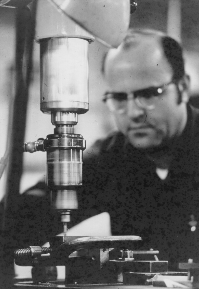 Man sitting behind a drill press.