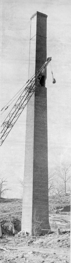 Crane with wrecking  ball in front of a brick chimney tower