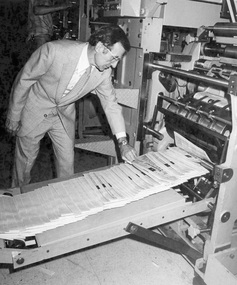 A man looking at newspapers coming off the printing press.