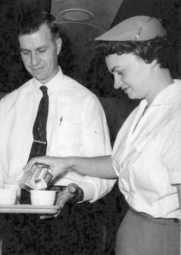 Woman pouring cream into coffee cup held on a tray by a man.