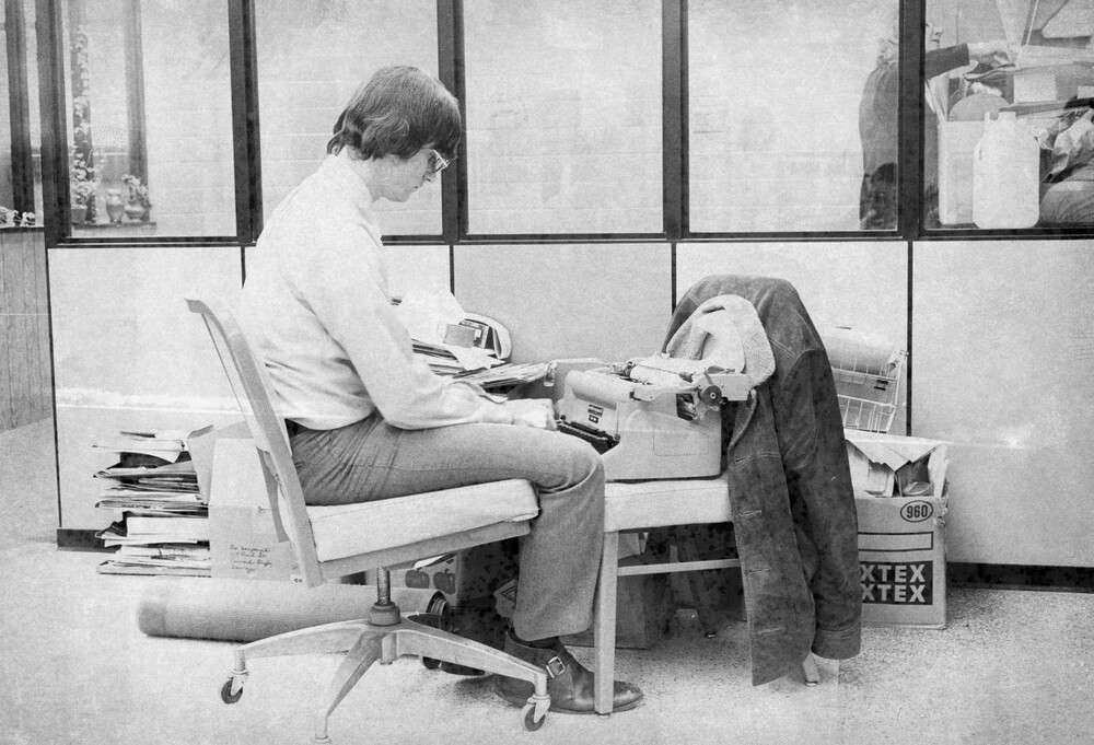 A man sitting in a chair looking at a typewriter.
