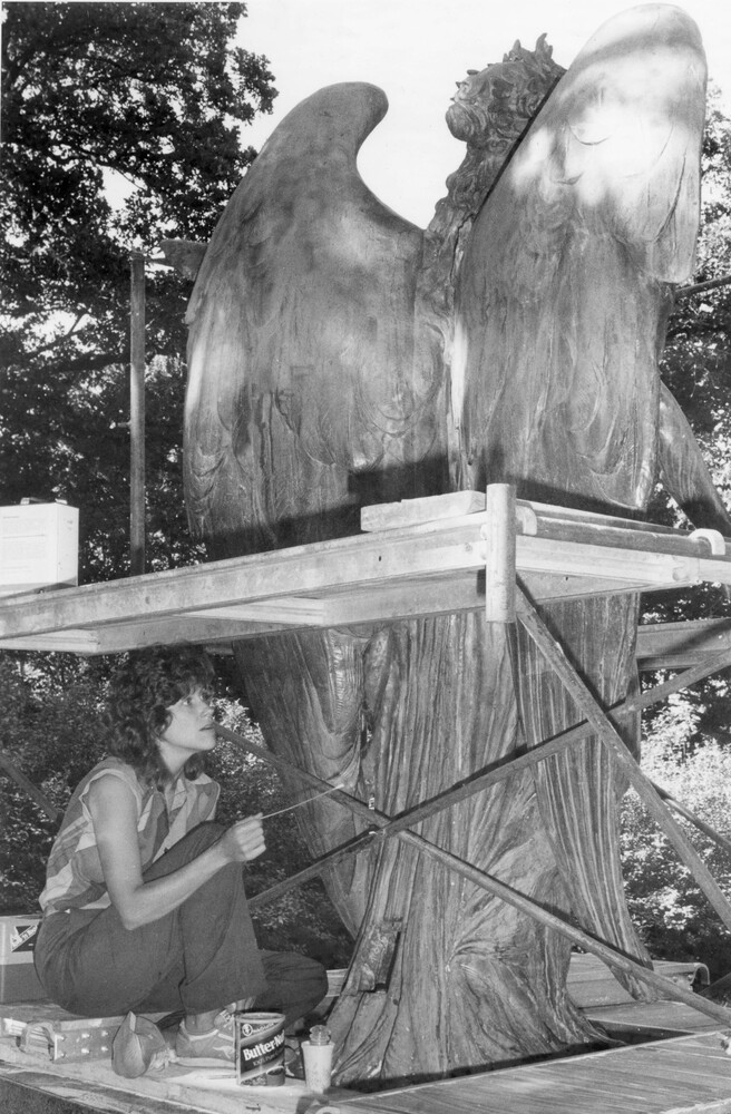 woman sitting under scaffold erected behind a large statue of an angel