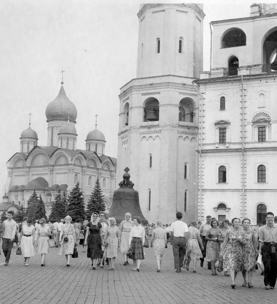 Tourists strolling brick street with large buildings in the background.