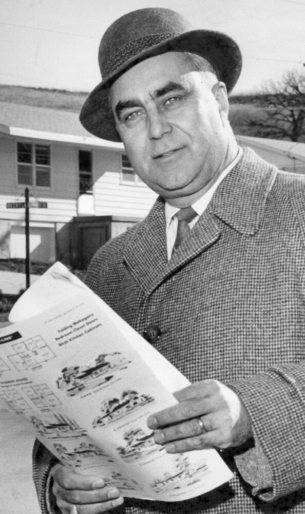 man in overcoat in hat holds several pages of paper