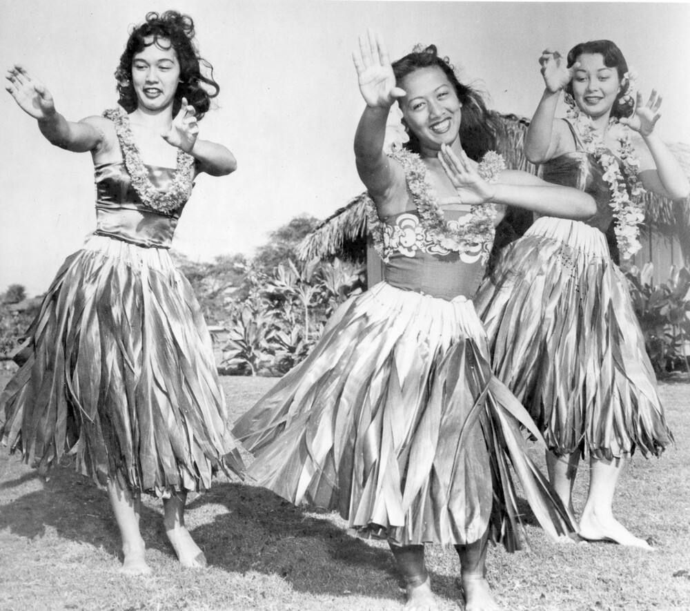 Three dancing women in grass skirts and leis.