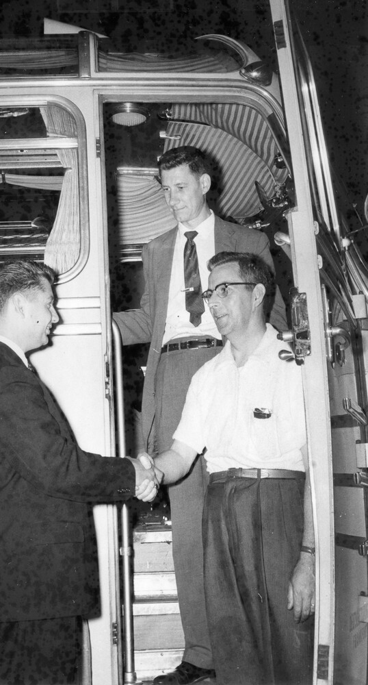 Two men shaking hands while another looks on.