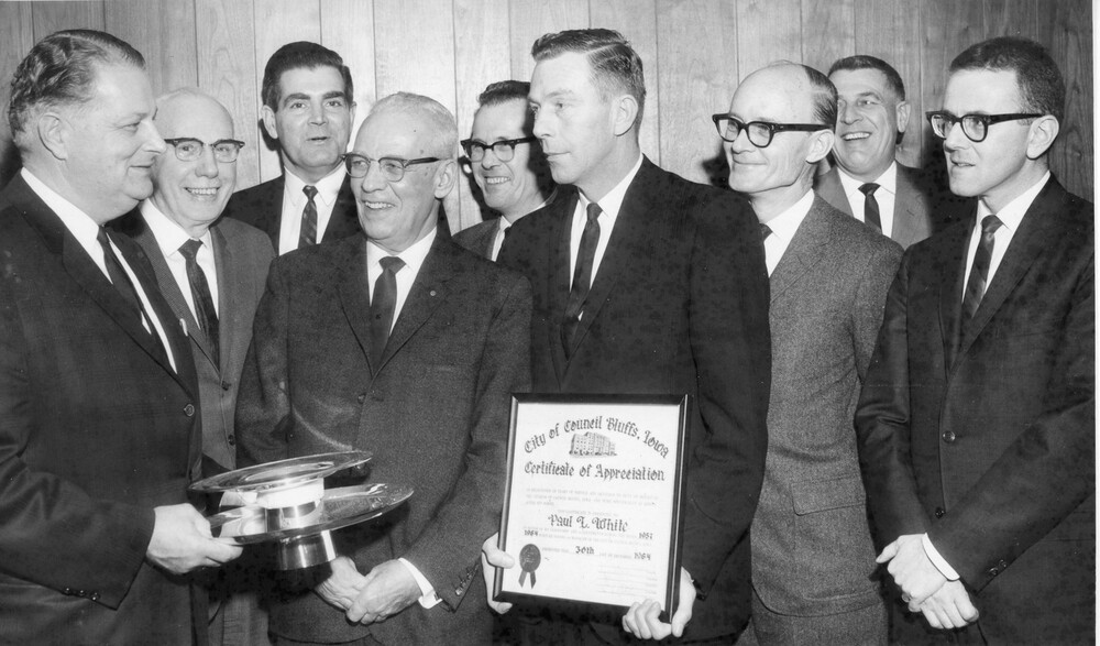 Man holding certificate appreciation, surrounded by eight other men