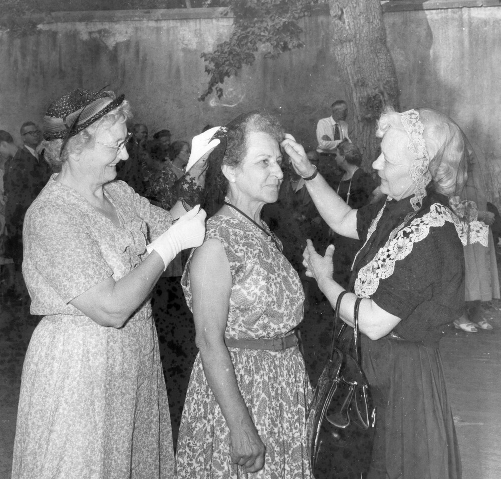 Two women adjusting the chapel veil of another woman. 