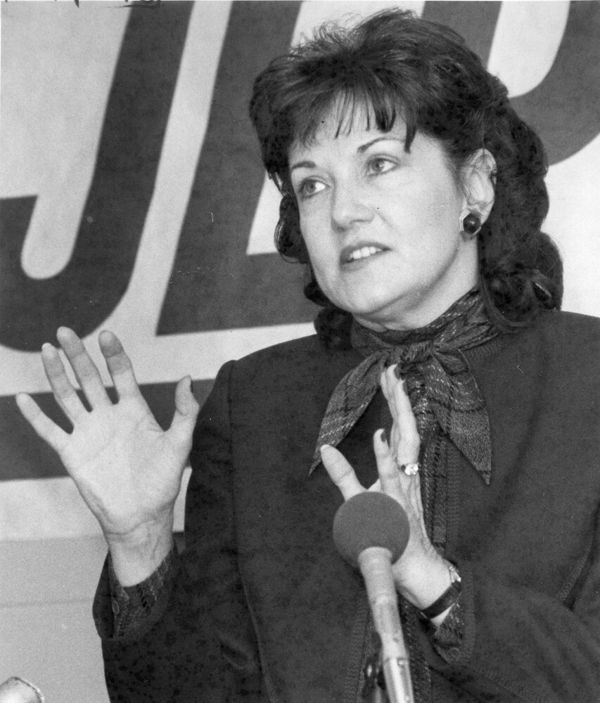 Woman stands behind microphone, gesturing with hands