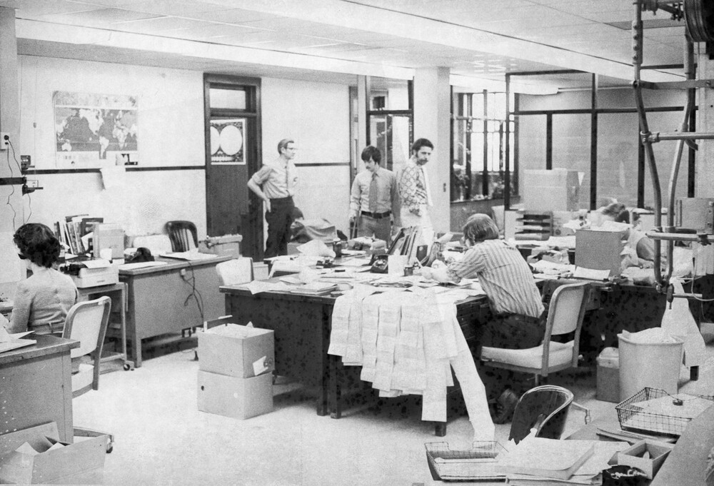 Four men looking at messy desks.