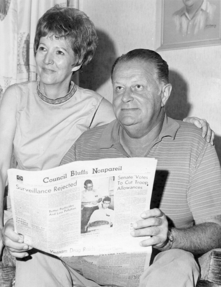 Man holding newspaper, woman beside him with arm around his shoulder