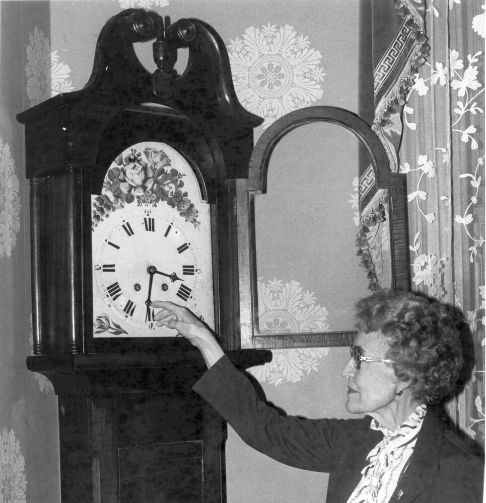 Woman setting the hands of an antique grandfather clock.