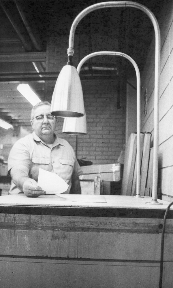 A man holding a piece of paper on a table under two lamps.