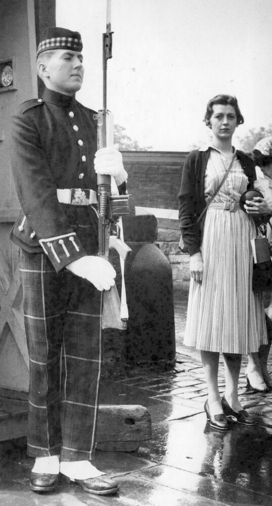 A woman standing near a uniformed guard with a rifle.