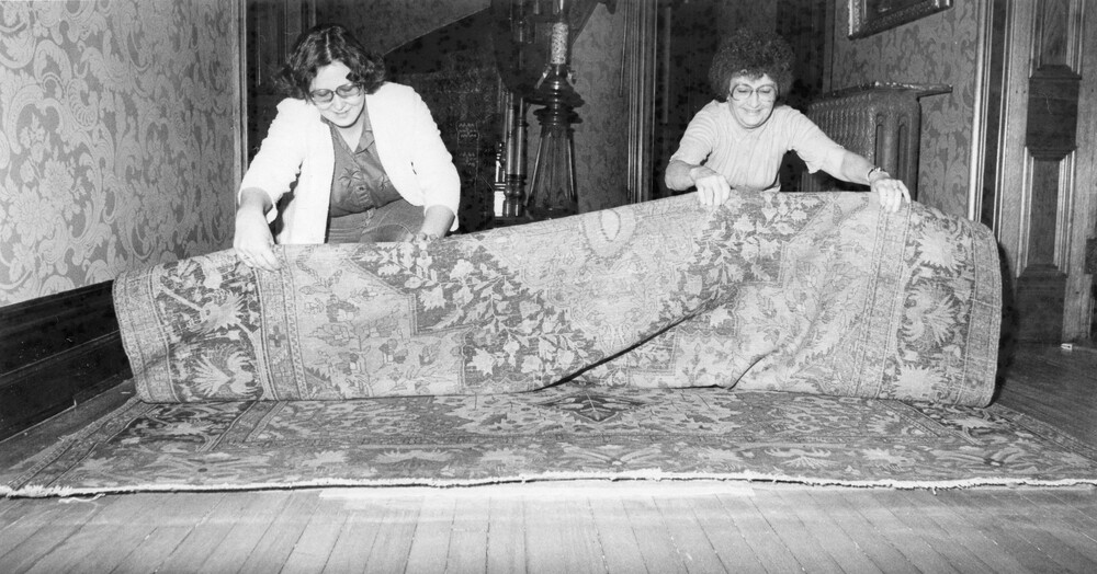 Two women rolling up a large, Persian-style rug.
