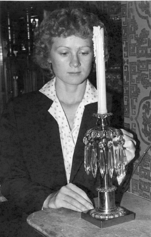 Woman stands behind antique candleholder with crystal tear drops.
