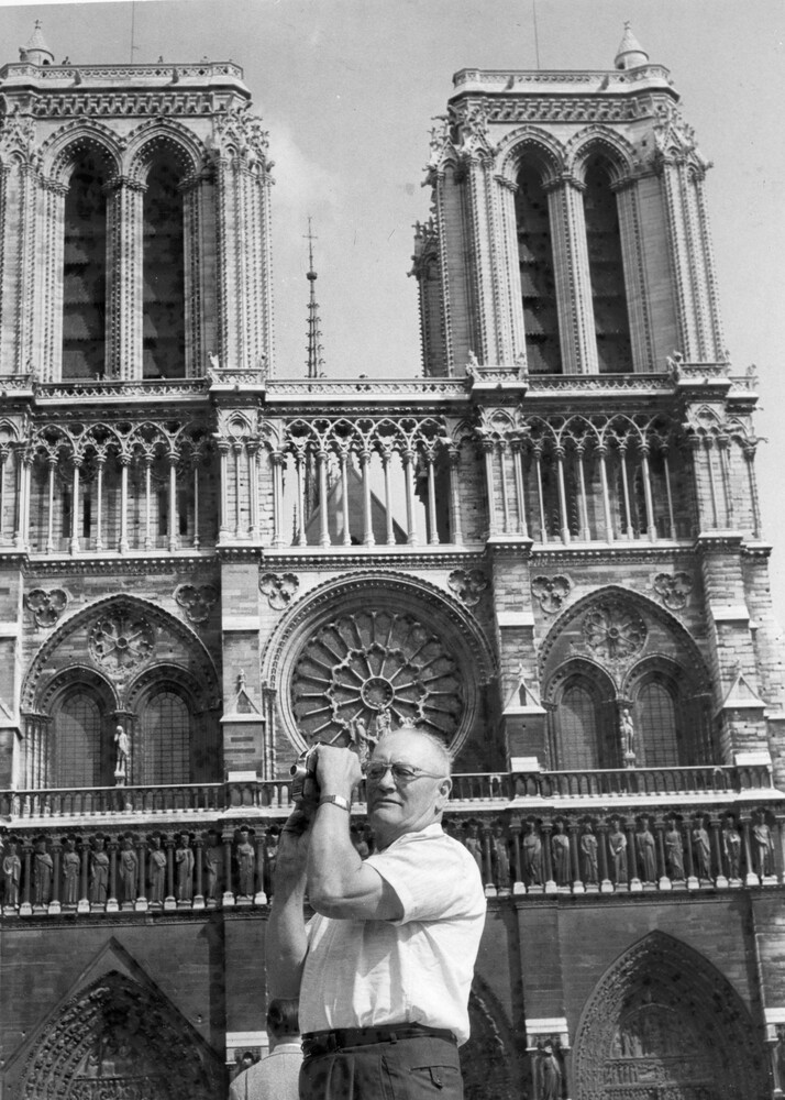 A man with a movie camera in front of a church.