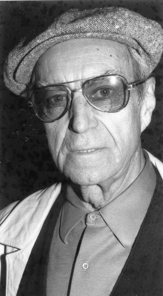 Head shot of older man wearing glasses and a cloth cap