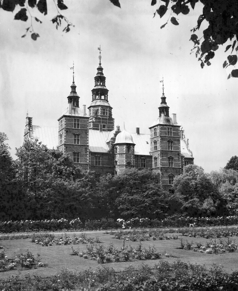A castle surrounded by trees and flower gardens.