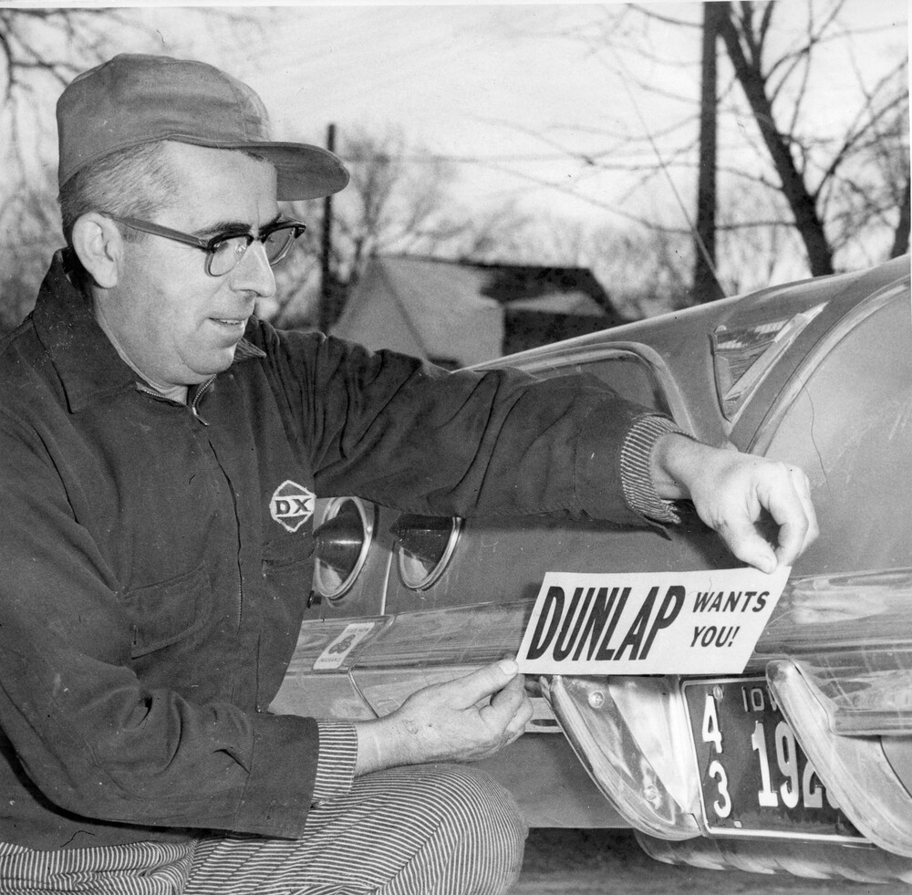 Kneeling man holds bumper stick next to a car's bumper
