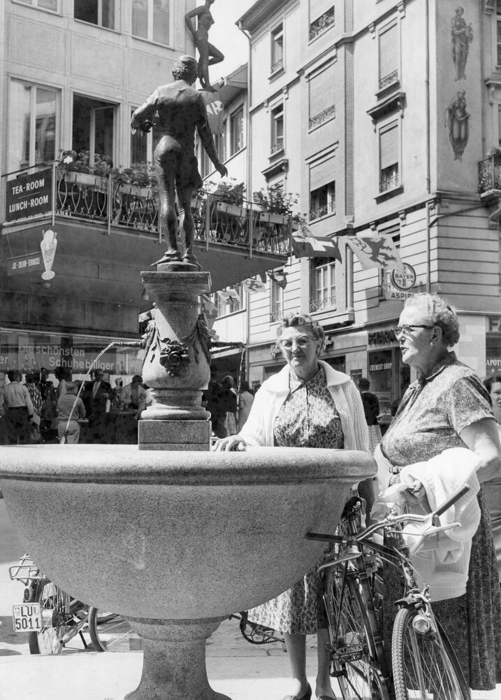 Two women at a fountain on a street.