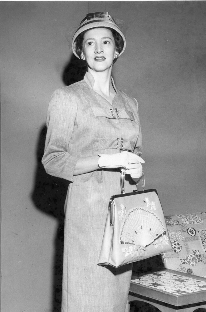 Woman models dress and jacket, cloche hat, and purse