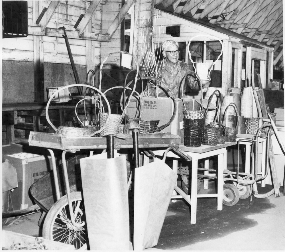 Older man standing by a variety of items, including baskets and dolleys/trolleys.