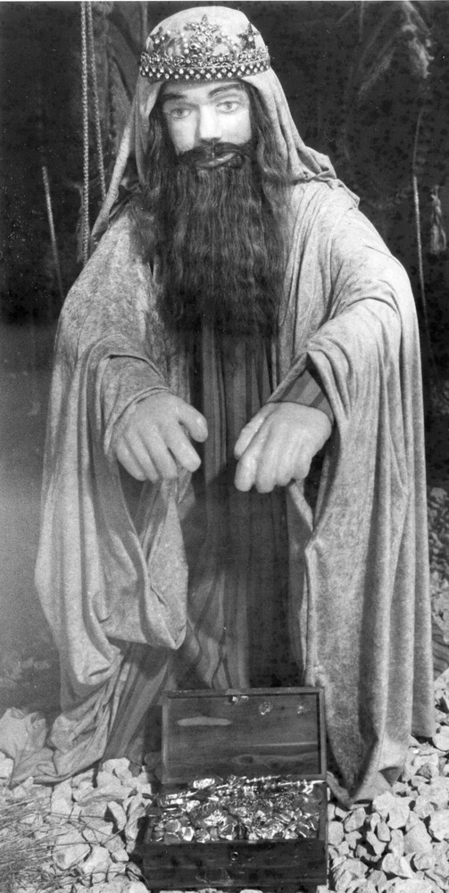 photo of wax figure dressed in robes, with box of gold coins