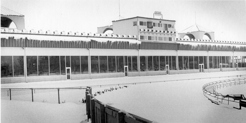 winter view of long building with many windows and doors, overlooking turn of a reacetrack