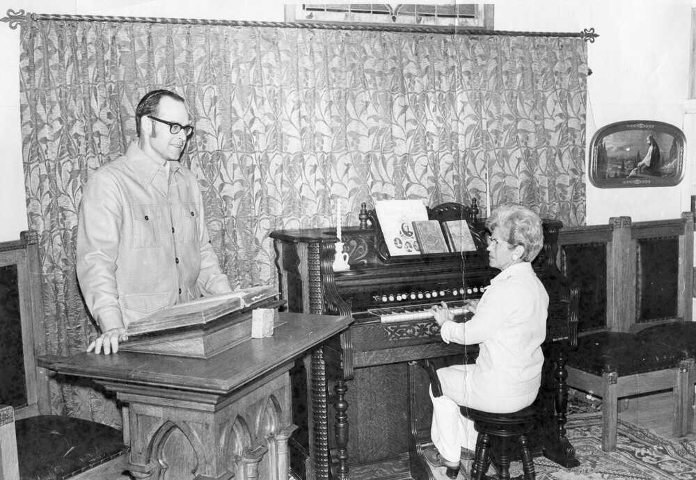 A man standing behind a pulpit and a woman playing an organ. 
