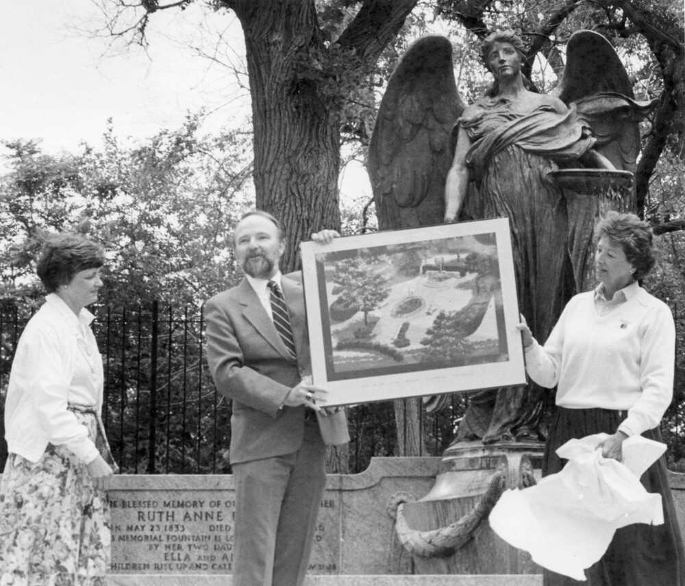 man presenting framed print in front of large outdoor state of an angel