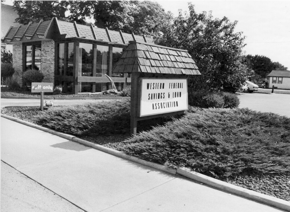 brick and glass building, sign with shingled top, and landscaping