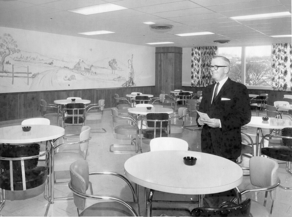 Man standing in a room with dining tables and chairs.