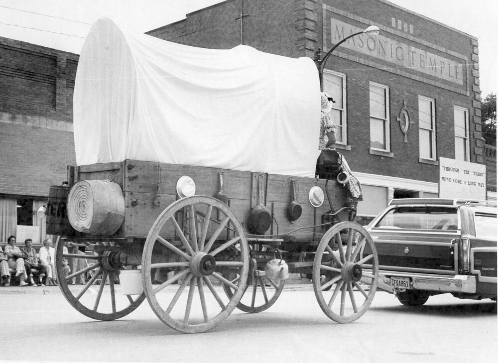 A covered wagon being pulled by a car.