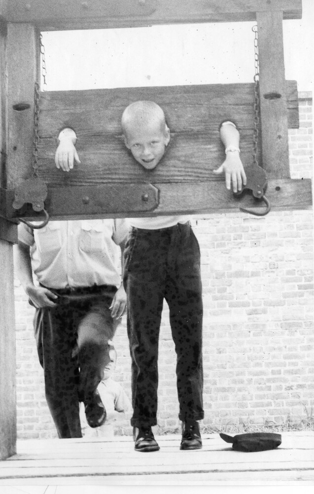 A smiling young man in a stock at a tourist attraction.