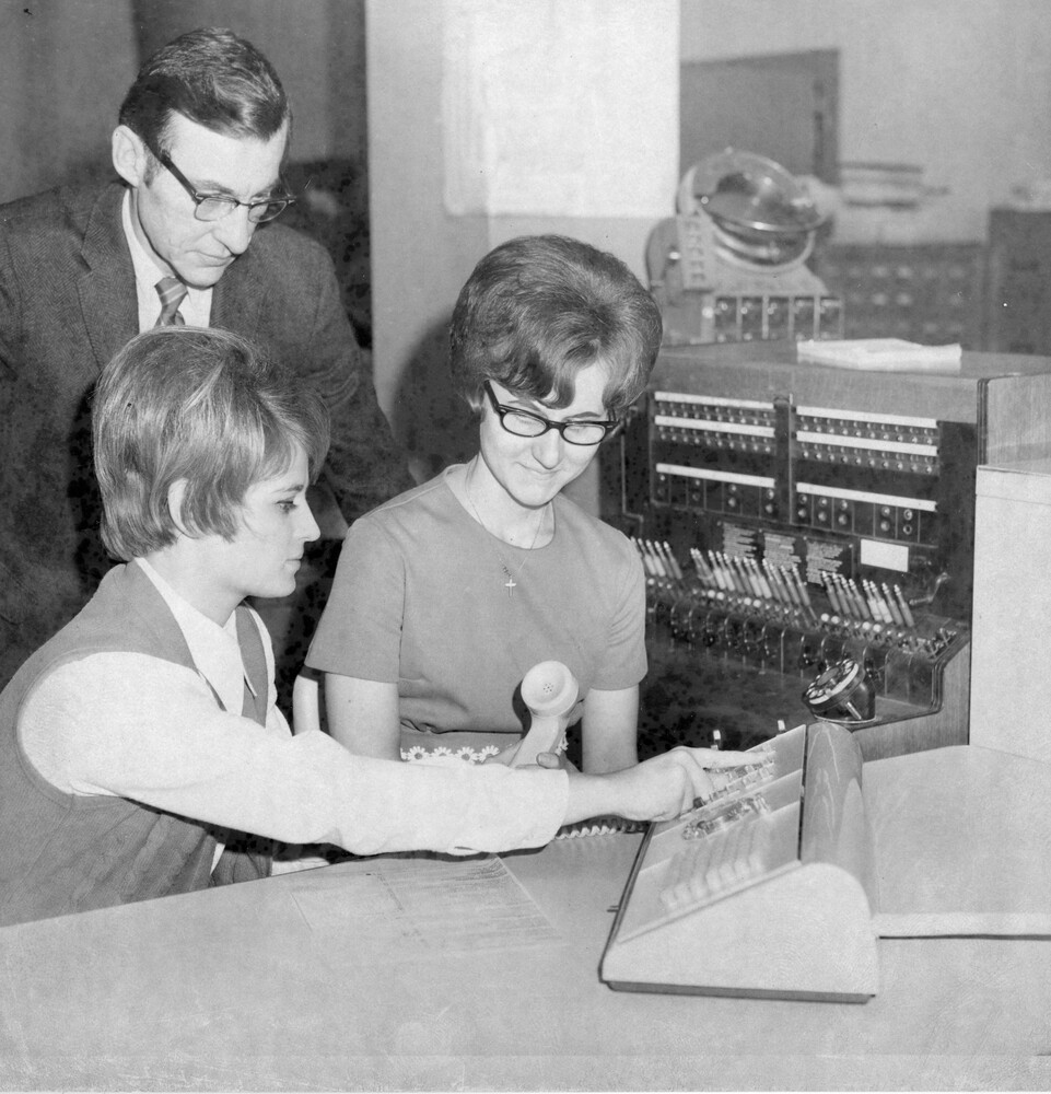 A man and two women viewing a telephone.