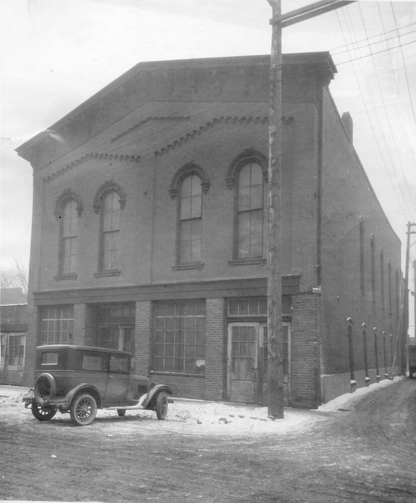 Exterior, front, of two-story brick building with Model T car parked in front.<br />

