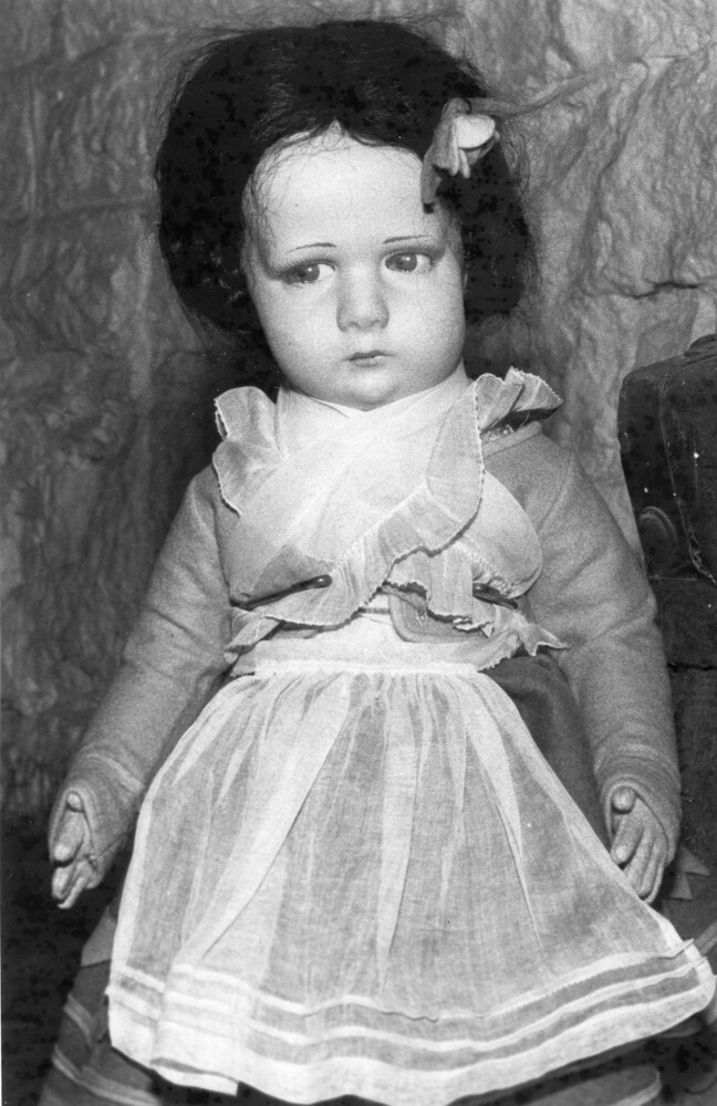 Antique girl doll with dark hair, wearing an apron.