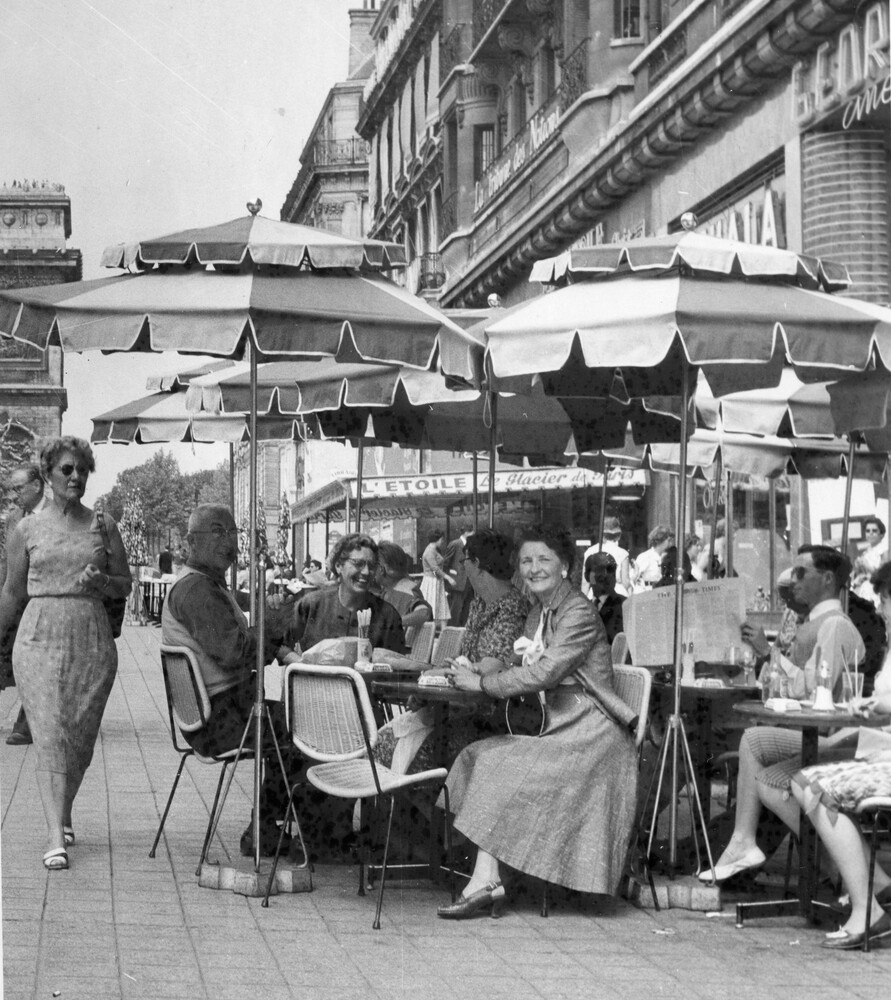 Tourists sitting under umbrellas at a sidewalk cafe.