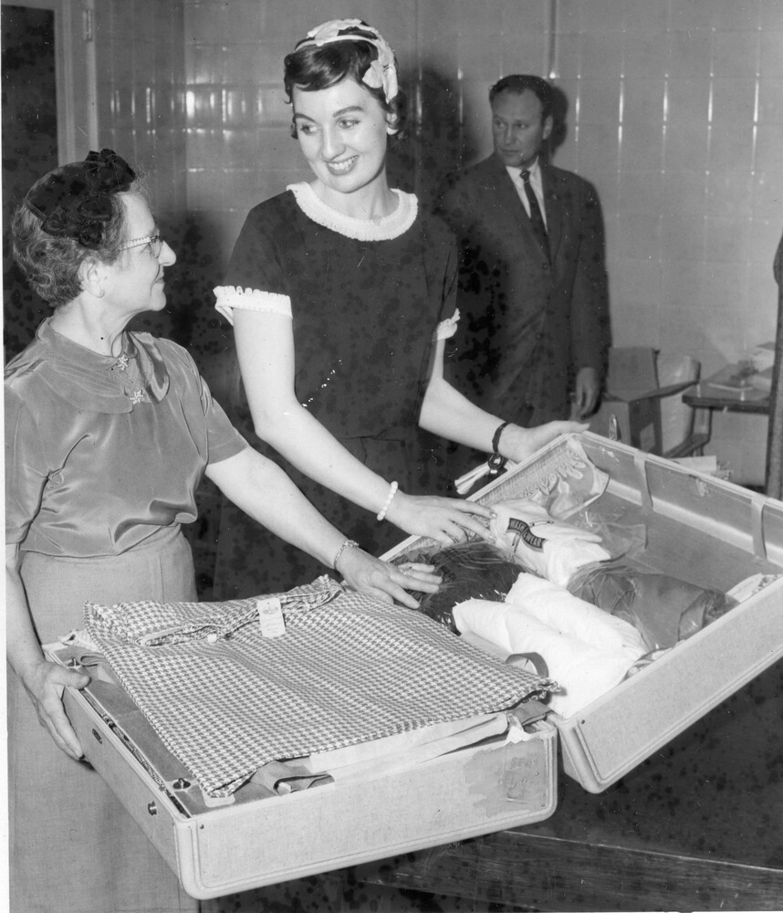 Two women with an open packed suitcase. Man in background.